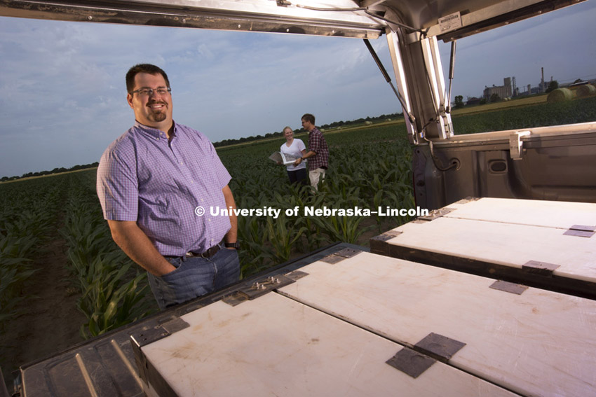 Trenton Franz and his cosmic ray detector in the back of a pickup truck.  He uses the detector to measure the moisture content of crop fields. With his is graduate students William Avery and Catherine Finkenbiner. June 24, 2015. Photo by Craig Chandler/University Communications.