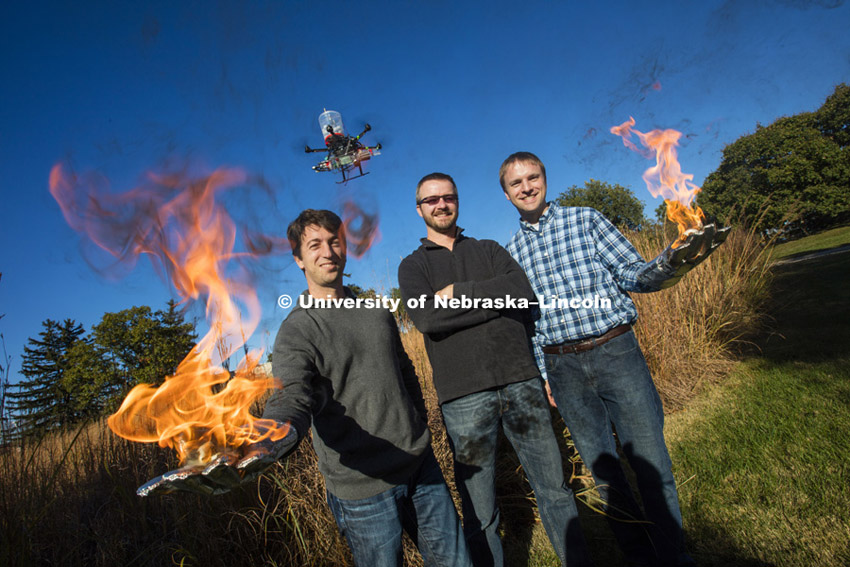Sebastian Elbaum, left, Dirac Twidwell and Carrick Detweiler are on fire with their new patent for setting range fires with small drones. Elbaum and Detweiler hold flaming table tennis ball similar to the ones carried by the drone flying above them. The drone injects a liquid into the plastic spheres to start a delayed fiery process so the balls can fall to the ground before igniting. Elbaum and Detweiler are professors of computer science and engineering. Twidwell is an assistant professor and gangland ecologist in the school of natural resources. October 29, 2015. Photo by Craig Chandler / University Communications