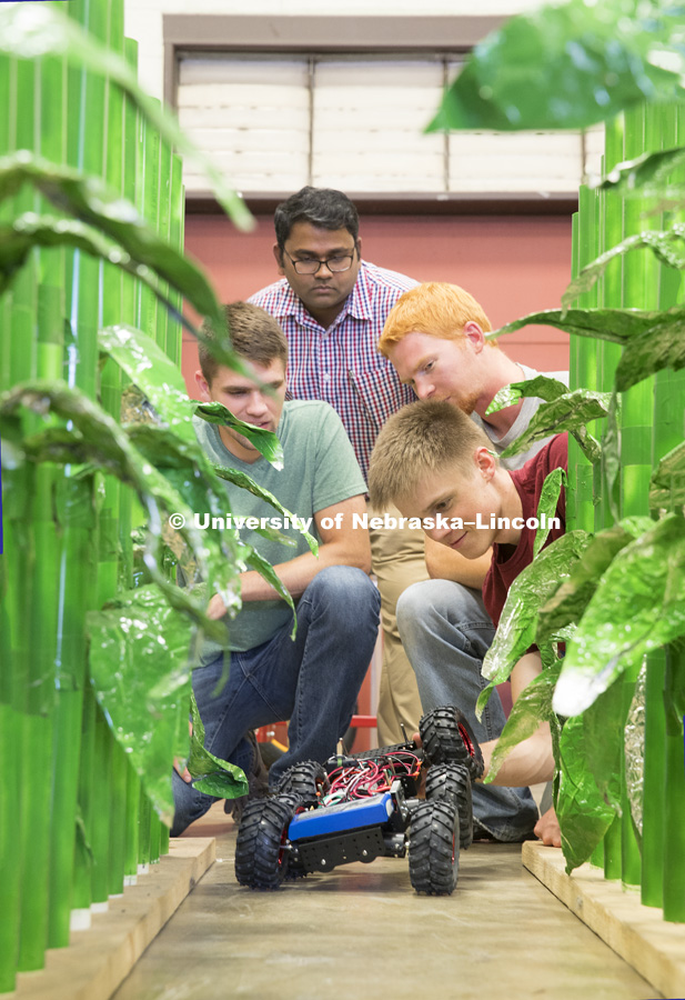 Lukas Renker, senior in Mechanical Engineering, prepares a robotic vehicle which is being developed to count seedlings in a corn row to measure germination. Professor Santosh Pitla, Tyler Troyer, graduate student in BSE, and Ethan Nutter, graduate student in mechanized systems management, are in the background. Robotics lab on east campus.  Biological Systems Engineering. August 15, 2016. Photo by Craig Chandler / University Communication.