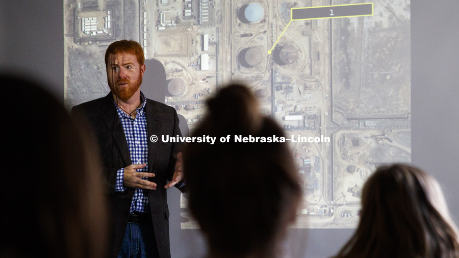 Tyler White, teaches while illuminated by a large satellite image of an Iranian oil refinery. Part of the UHON 395H - University Honors Seminar is learning how information is obtained by such imagery. November 28, 2016. Photo by Craig Chandler / University Communication.