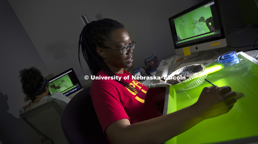 Imani Brown and Thalia Rodgers, both FPA students from Omaha, paint on a "green screen" lightbox. A computer screen shows an image of Thalia Rodgers’ hand and brush as she creates an animation by painting over a live-action scene with a technique called