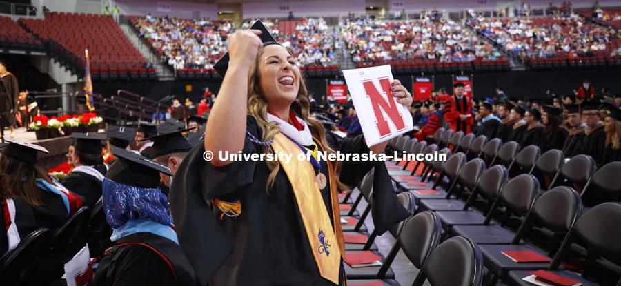 Alexandria Leavenworth gestures to her family and friends in the arena audience after receiving her masters in journalism and mass communication. Students earning graduate and professional degrees received their diplomas Friday afternoon in Lincoln's