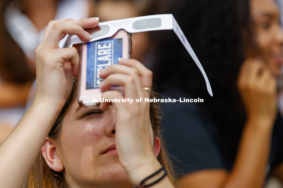 A student uses her glasses as a filter for her phone's camera at 12:56 pm as the final edge disappears behind the moon. Students gather on the green space between the Nebraska Union and the Raikes School to view the solar eclipse. August 21, 2017. Photo