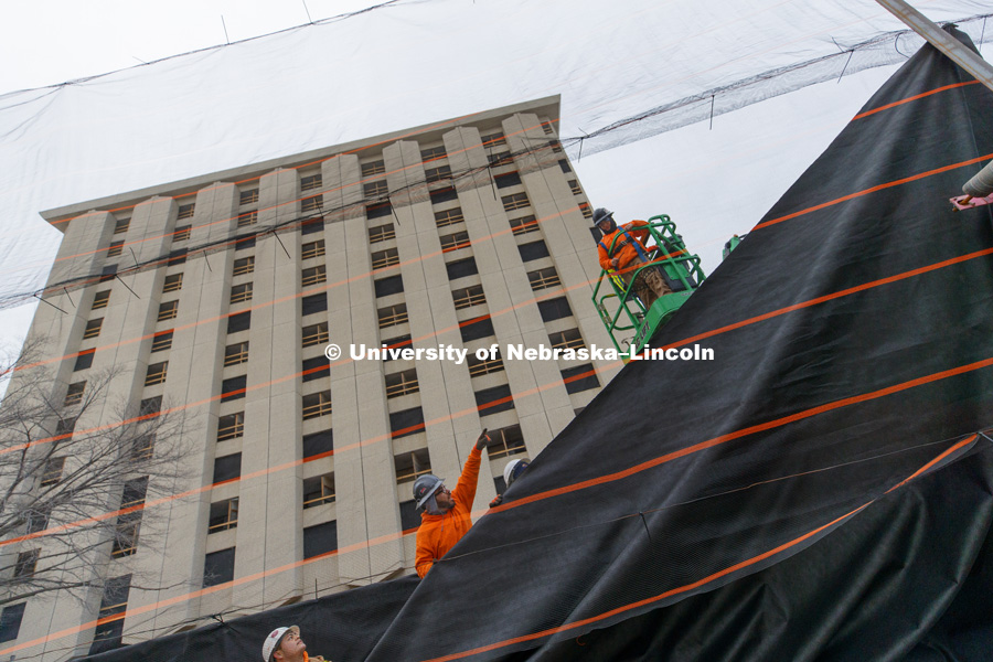 Worker with Ark Wrecking hang fabric over a mesh wall erected along 17th street in Lincoln. The wall will keep any dust and debris from the Cather Pound implosion from reaching the Knoll Residence Hall and Willa Cather Dining Center across the street from