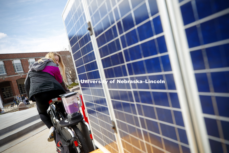 Julia Dirkse eyes her smoothie she is making using a bicycle-powered blender at the Campus Rec booth.  At right is a display of solar panels and solar cells. Environmental Sustainability Committee (ESC) is hosting its 4th annual Earthstock: Four Weeks to
