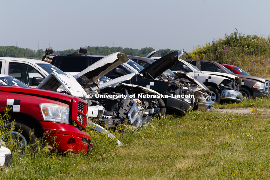 Rows of previous test cars and trucks sit behind the facility. Test of bull-nose barrier for use in medians to protect cars from overpass columns. Test was at university's Midwest Roadside Safety Facility at the Lincoln airport. June 5, 2018. Photo by