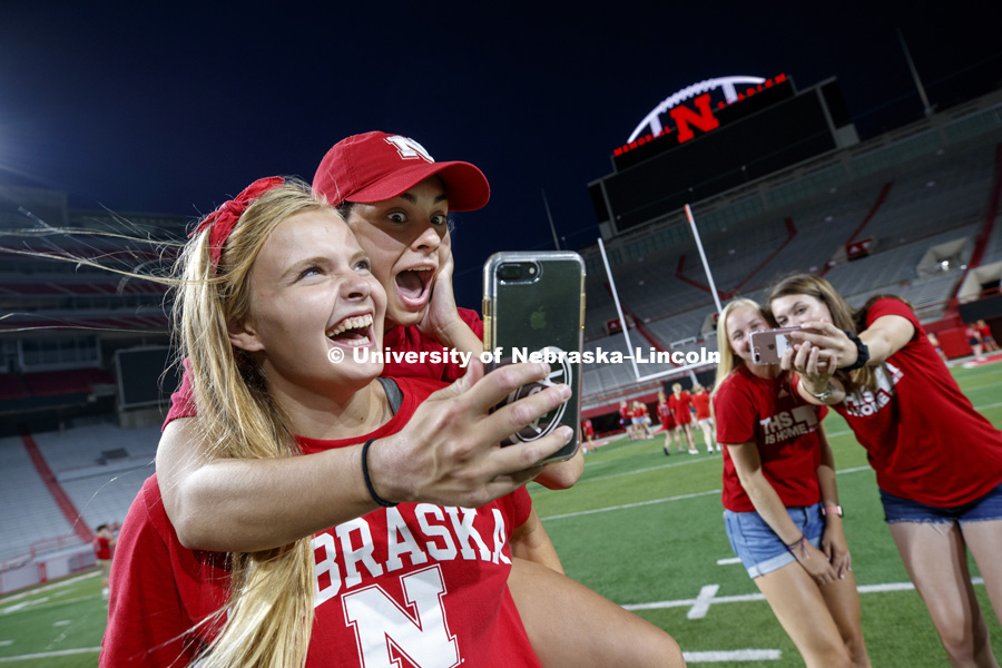 Carly Howrey of Hospers, Iowa, and Rachel Dempsey of Omaha take selfies on the field following the tunnel walk for incoming students. August 17, 2018. Photo by Craig Chandler / University Communication.