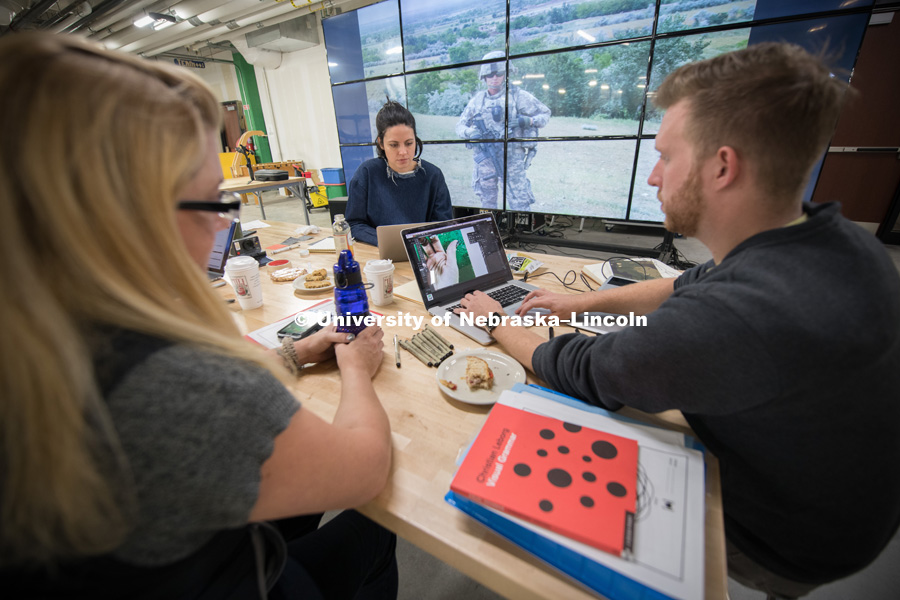 Veteran Melissa Ewing (left), Kendra Clapp Olguin, Has Heart communications director, and Husker alum Jordan Lambrecht work on the artwork representing Ewing's life story. Behind them, on screens at Nebraska Innovation Studio, is a photograph from Ewing's tour in Afghanistan. October 12, 2018. Photo by Greg Nathan, University Communication.