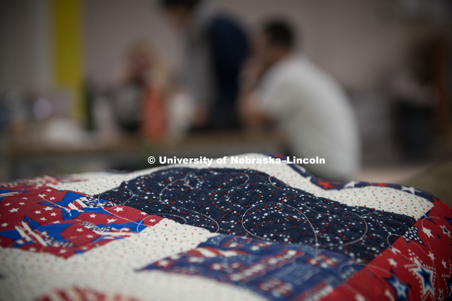 Pictured; Patriotic quilt. Veteran Melissa Ewing (left), Kendra Clapp Olguin, Has Heart communications director, and Husker alum Jordan Lambrecht work on the artwork representing Ewing's life story. Behind them, on screens at Nebraska Innovation Studio, is a photograph from Ewing's tour in Afghanistan. October 12, 2018. Photo by Greg Nathan, University Communication.