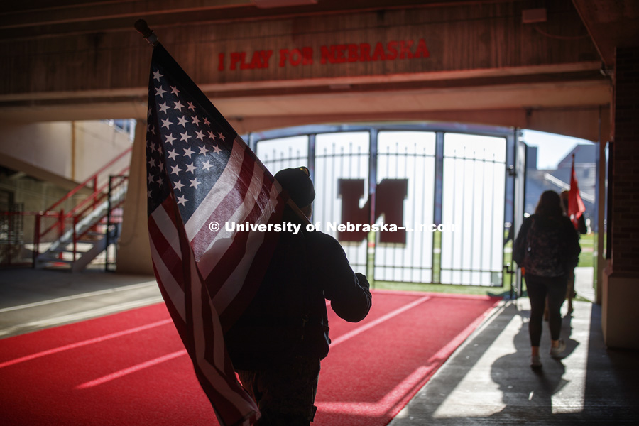 Jerod Post, '13 and a Marine veteran, carries the US flag into Memorial Stadium to the starting point of the Ruck March. Beginning of veterans Ruck March which uses Nebraska and Iowa veterans to carry the game ball from Lincoln to Iowa City. November 14, 2018. Photo by Craig Chandler / University Communication.