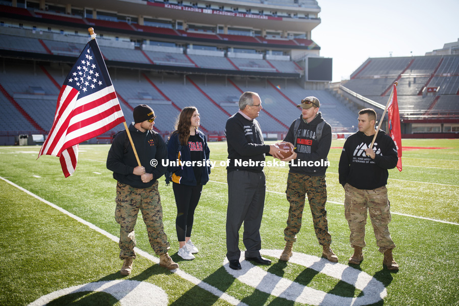 Jerod Post, '13 and a Marine veteran, and undergraduate Natalie Kraft, a Navy veteran, watch as Athletic Director Bill Moos presents the game ball to undergraduate and Marine veteran Jake Post. At right is undergraduate and Army veteran Jared Collins. Beginning of veterans Ruck March, which uses Nebraska and Iowa veterans to carry the game ball from Lincoln to Iowa City. November 14, 2018. Photo by Craig Chandler / University Communication.
