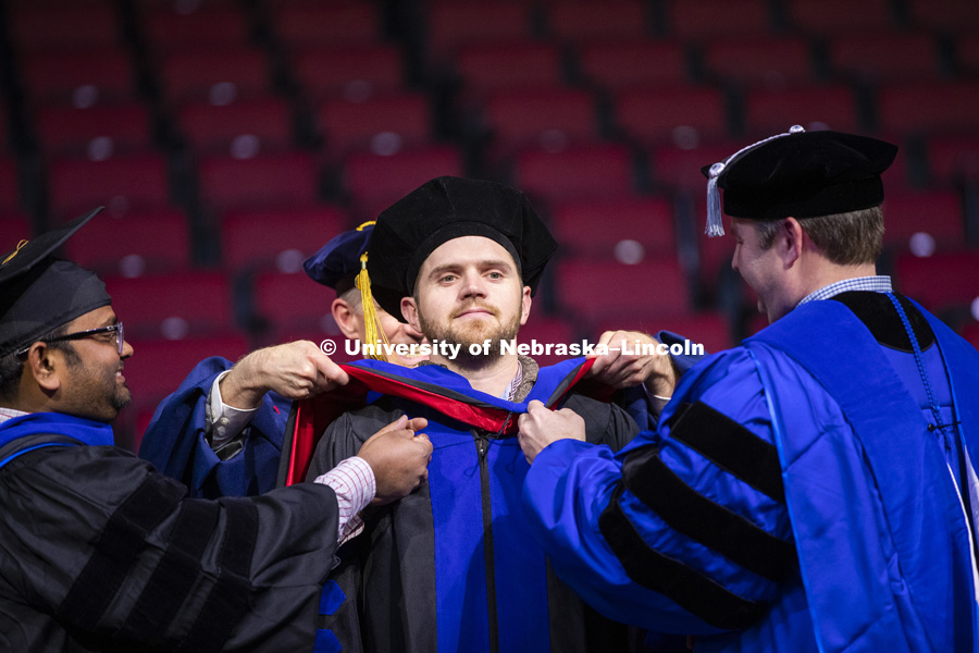 John Evans, Phd in Biological Engineering, has his doctoral hood placed over his head by Professors Santosh Pitla and Joe Luck at the Graduate Commencement and Hooding in Pinnacle Bank Arena. December 14, 2018. Photo by Craig Chandler / University Communication.