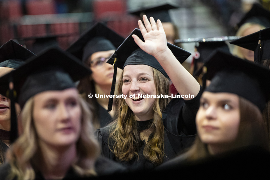 Delaney McFadden waves to her family and friends after taking her seat on the arena floor at the Undergraduate Commencement in Pinnacle Bank Arena. December 15, 2018. Photo by Craig Chandler / University Communication.