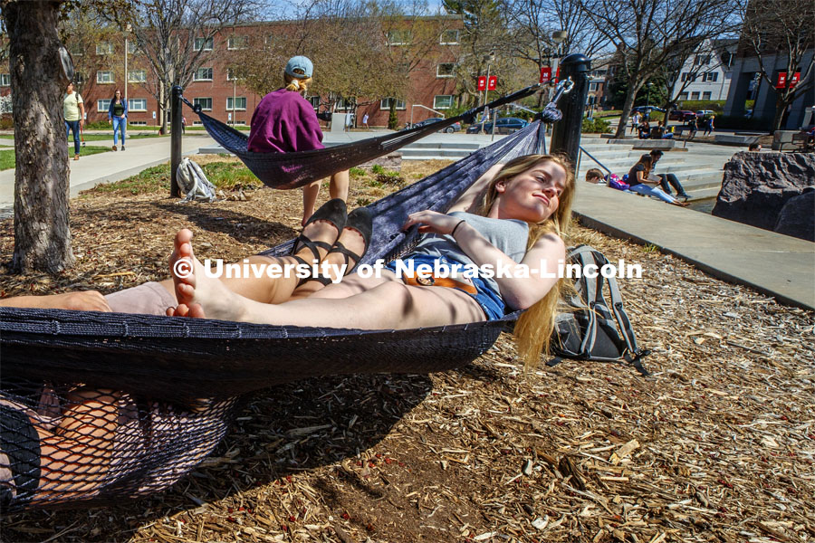 Sammy Cope, freshman from Omaha, enjoys the sunshine as she and Calli Mah, freshman from Mitchell, South Dakota, hang out in the hammocks by the Broyhill fountain. Spring Day on City Campus. April 9 2019. Photo by Craig Chandler / University Communication.