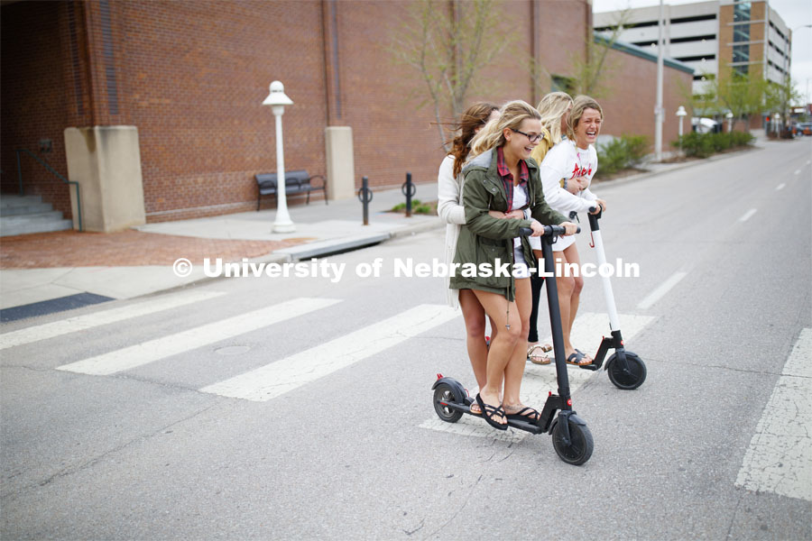 Four students roll onto campus riding electric scooters. April 22, 2019. Photo by Craig Chandler / University Communication.