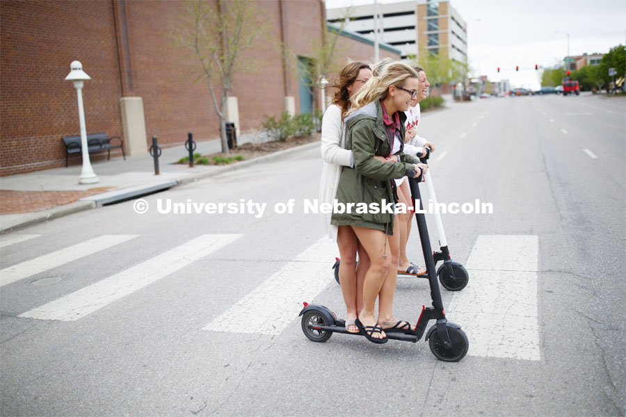 Four students roll onto campus riding electric scooters. April 22, 2019. Photo by Craig Chandler / University Communication.