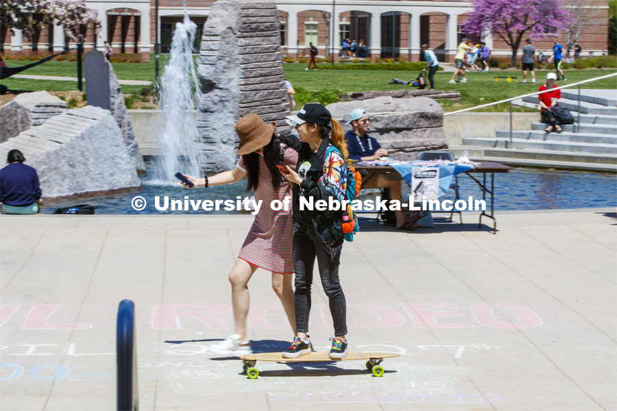 Hanchen Zhang gets a free ride on her skateboard as her friend, Sihui Li walks her along the plaza by the fountain. April 24, 2019. Photo by Craig Chandler / University Communication.
