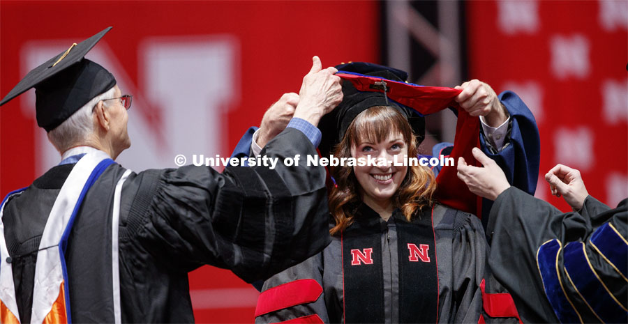 Ariel Setniker ducks under her doctoral hood as it's lowered over her head. 2019 Spring Graduate Commencement in Pinnacle Bank Arena. May 3, 2019. Photo by Craig Chandler / University Communication