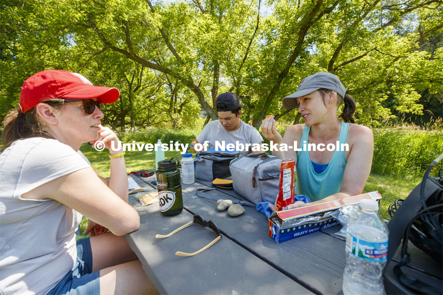Kayla Vondracek talks with Professor Jessica Corman as they and Matthew Chen take their lunch break riverside. Professor Jessica Corman prepares more filtered water. Jessica Corman, assistant professor in the School of Natural Resources, UCARE research group researching algae in the Niobrara River. Fort Niobrara National Wildlife Refuge. July 12, 2019. Photo by Craig Chandler / University Communication.