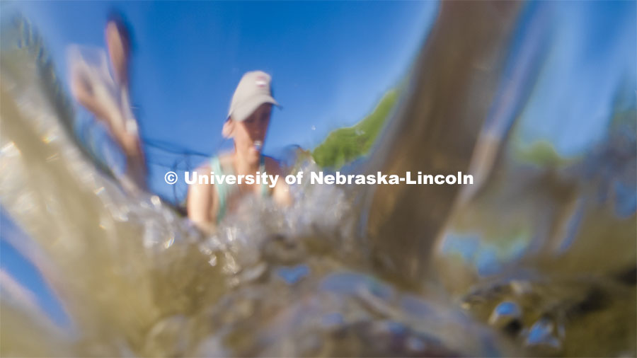 Kayla Vondracek, junior in Environmental Studies, fights the current and depth to take a sand sample as she researches algae in the Niobrara River. Jessica Corman, assistant professor in the School of Natural Resources, UCARE research group researching algae in the Niobrara River. Fort Niobrara National Wildlife Refuge. July 12, 2019. Photo by Craig Chandler / University Communication.