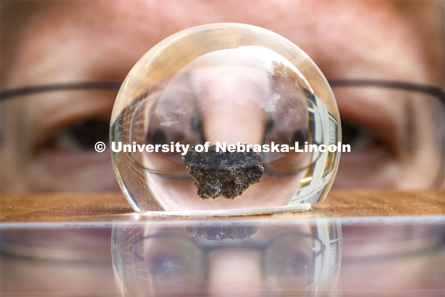 A rock collected from Apollo 17's 1972 lunar landing is held by Joel Nielsen, Graphics Specialist and Project Coordinator at the University of Nebraska State Museum, Morrill Hall. It is encased in acrylic and is part of a plaque that also displays a small Nebraska flag that traveled to the moon and back. Moon rocks at University of Nebraska State Museum. July 16, 2019. Photo by Craig Chandler / University Communication.