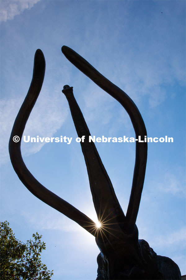 The sun peeks past Archie the mammoth sculpture outside of Morrill Hall. City Campus. September 17, 2019. Photo by Craig Chandler / University Communication.