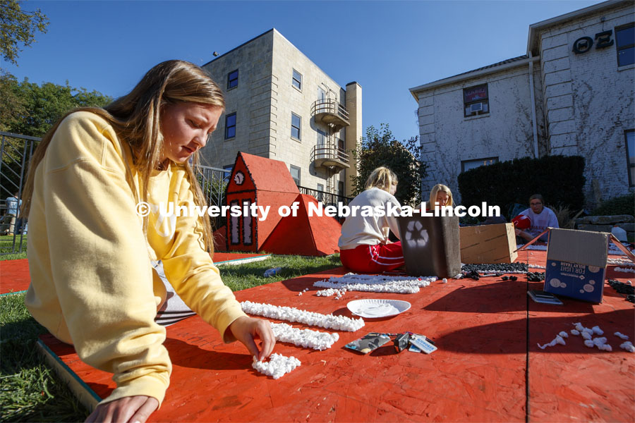 Anna Heinrich, freshman from Lincoln, glues poms to a plywood display outside the Theta Xi house. Students from Theta Xi, Alpha Phi, Kappa Alpha Theta, Phi Kappa Theta work on their homecoming display. 2019 Homecoming display decorations. October 3, 2019. Photo by Craig Chandler / University Communication.