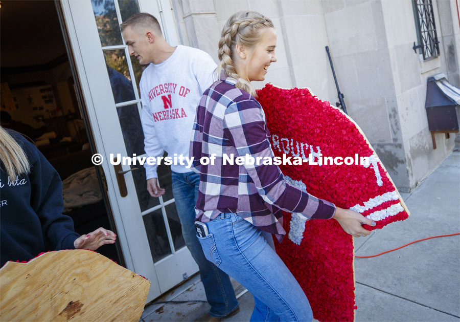 Willa Scoville, freshman from Hartington, NE, carries out a decorated football jersey for the homecoming display outside the Alpha Tau Omega house. Students from Alpha Tau Omega, Gamma Phi Beta, Delta Delta Delta, Acacia, Sigma Alpha Mu work on their display. 2019 Homecoming display decorations. October 3, 2019. Photo by Craig Chandler / University Communication.