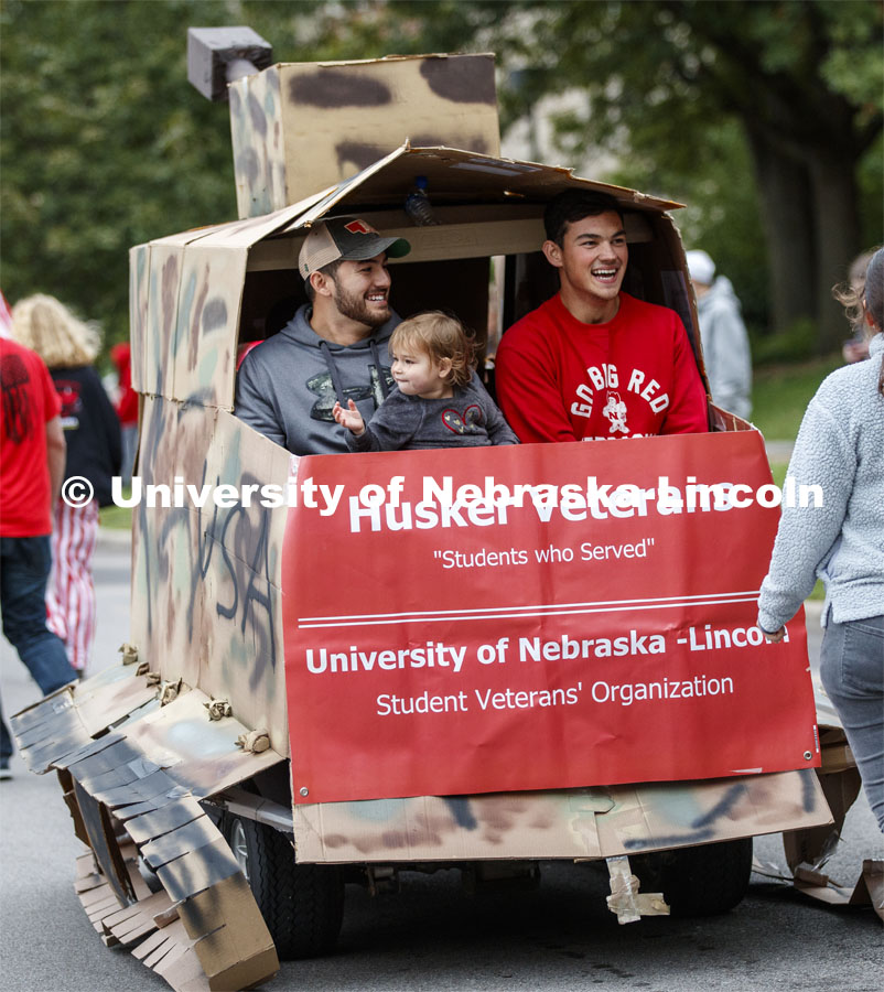 Lorelai Dingman, 2, shares a ride with Marine veterans and second year students Rodrigo Venegas, left, and Jessi Meyer share the back of the Student Veterans' Organization golf cart decorated as a tank. Cornstock celebration and Homecoming Parade. October 4, 2019. Photo by Craig Chandler / University Communication.