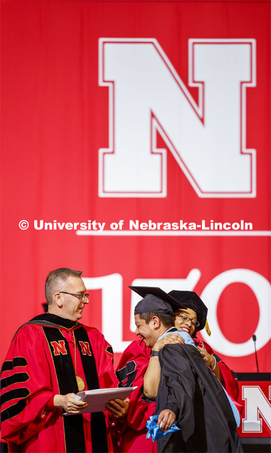 Hector de Jesus Palala Martinez is hugged by Marshall Marianna Banks as he receives his degree from Chancellor Ronnie Green. Graduate Commencement and Hooding at the Pinnacle Bank Arena. December 20, 2019. Photo by Craig Chandler / University Communication.