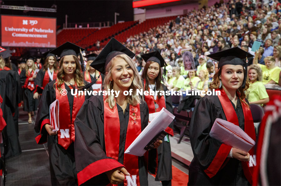 Alyssa Arndt smiles as she walks past her family cheering section. The family all wore neon green shirts so Alyssa wouldn't miss seeing them. December Undergraduate commencement at Pinnacle Bank Arena. December 21, 2019. Photo by Craig Chandler / University Communication.