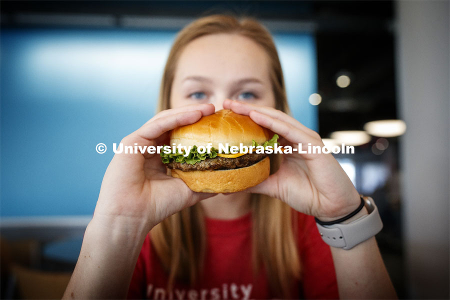Cather Dining Center photoshoot. Young woman holding a burger in front of her face. March 2, 2020 Photo by Craig Chandler / University Communication.