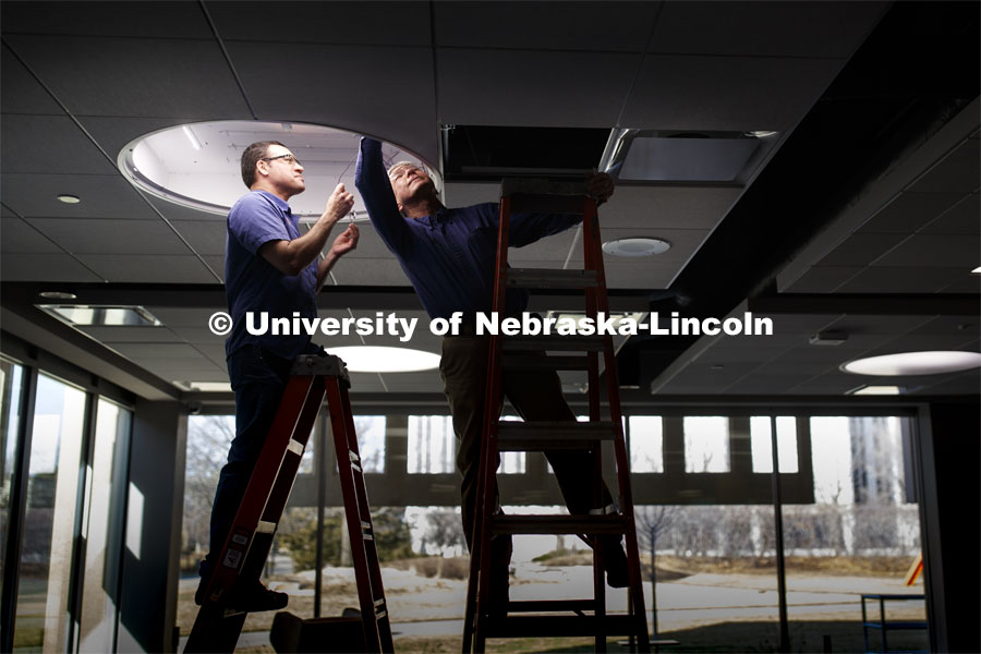 Marcelo Ortega and Doug Winkler with Facilities Management and Planning work to replace a light fixture in Love Library North, City Campus. March 17, 2020. Photo by Craig Chandler / University Communication.