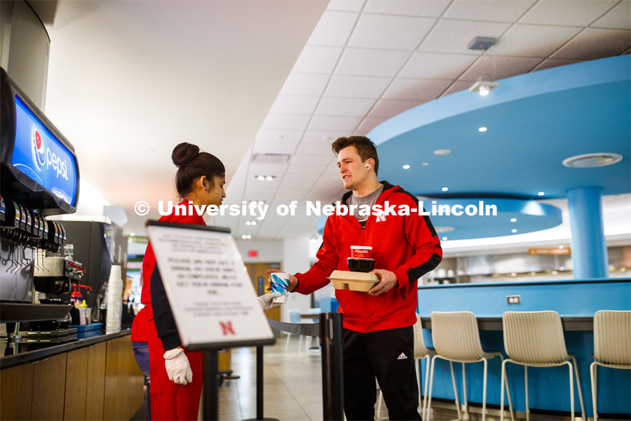 Zachery Borer, a freshman from North Bend, NE, collects his drink and lunch to-go from Manpreet Kaur in the Willa S. Cather Dining Complex on City Campus. March 17, 2020. Photo by Craig Chandler / University Communication.