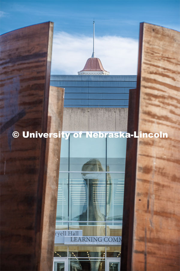 Mueller Bell Tower is reflected in the windows of Love Library, while being framed by the Greenpoint Statue. April 1, 2020. Photo by Craig Chandler / University Communication.