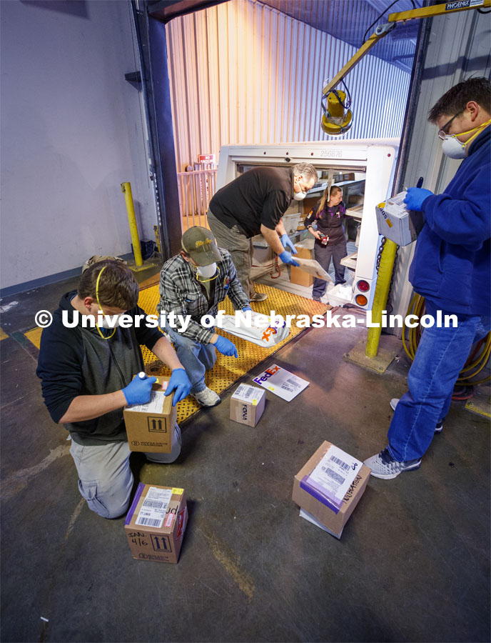 University employees sort packages after a morning delivery at the Facilities Management Shops on N. 22nd St. The facility has been set up to serve as a central distribution point for the majority of packages delivered to campus during the COVID-19 pandemic. There, the packages are sorted, logged in and the recipients notified to pick up the package or have it stored until they return. April 6, 2020. Photo by Craig Chandler / University Communication.