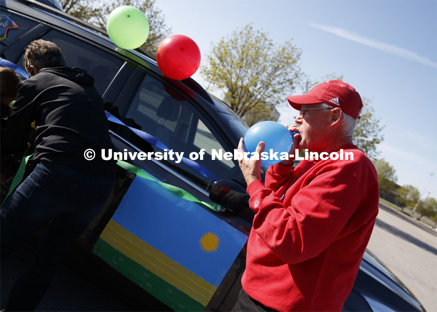 Ratch O'Connell blows up a blue balloon to decorate his vehicle.  Blue, yellow and green balloons and streamers, the national colors of Rwanda, along with Husker Red decorated many of the vehicles. Christ Place Church families gave the Rwandan students a vehicle parade to help celebrate the graduates and undergraduates. The church has been host families for about 25 of the 50 Rwandan students who are graduating. They also provided fall and spring event off-campus marking the beginning and ending of each school year along with rides from campus to church and back each Sunday. The group of host families had been planning a graduation party for the students until COVID-19 occurred. Because of COVID-19, the group has planned for a socially distanced “parade” of host family vehicles that circled University Suites on R Street. May 8, 2020. Photo by Craig Chandler / University Communication.
