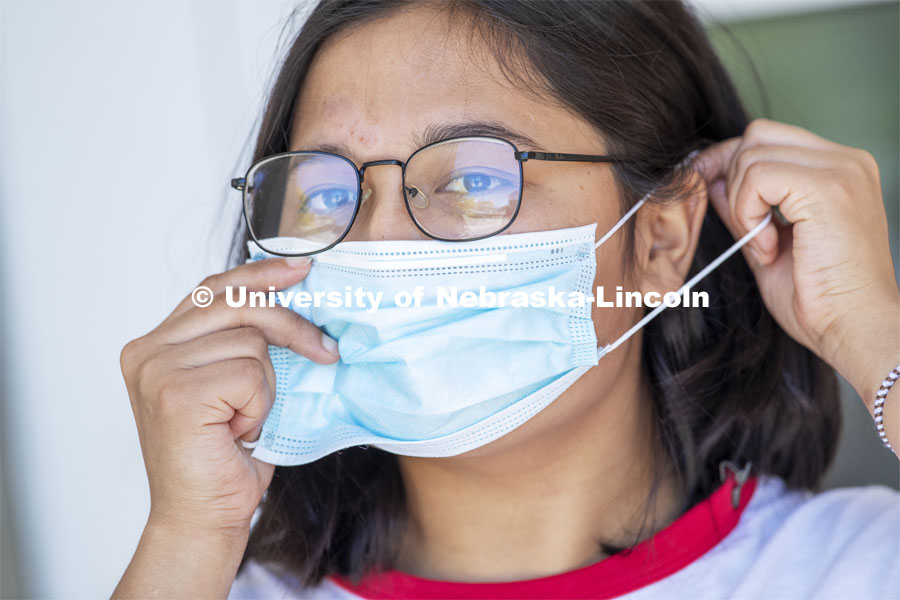 Sandhya Karki demonstrates how to put on a mask. Photo shoot of students wearing masks and practicing social distancing. June 24, 2020. Photo by Craig Chandler / University Communication.