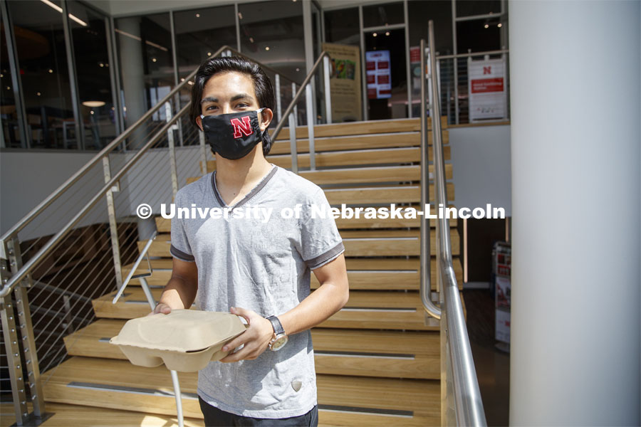 A young man wearing a Husker mask gets takeout dining from the Willa Cather Dining Center. Photo shoot of students wearing masks and practicing social distancing in dining services in Willa Cather Dining Center. July 1, 2020. Photo by Craig Chandler / University Communication.