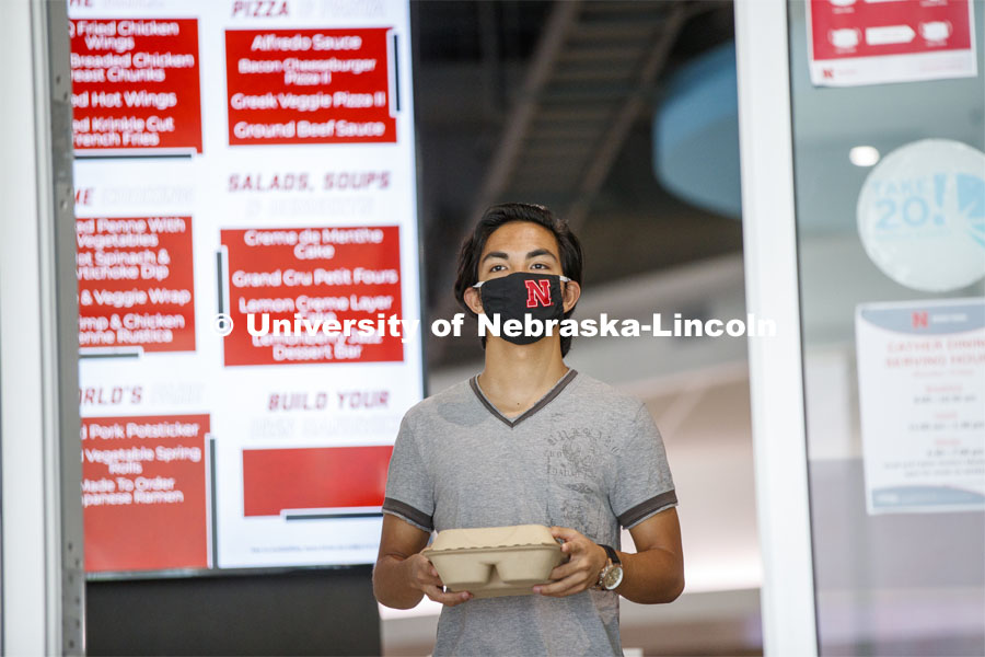 A young man wearing a Husker mask gets takeout dining from the Willa Cather Dining Center. Photo shoot of students wearing masks and practicing social distancing in dining services in Willa Cather Dining Center. July 1, 2020. Photo by Craig Chandler / University Communication.