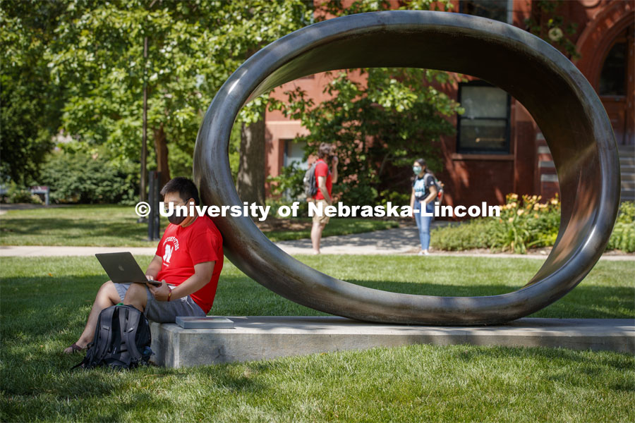 Photo shoot of students on city campus display mask wearing and social distancing. A young man sits and studies by the Fragment XO Sculpture as students cross campus near by.August 5, 2020. Photo by Craig Chandler / University Communication.