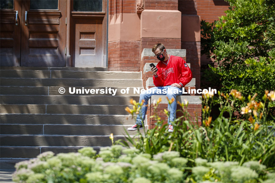 Photo shoot of students on city campus display mask wearing. A masked young man sits outside Richards Hall and checks his phone. August 5, 2020. Photo by Craig Chandler / University Communication.