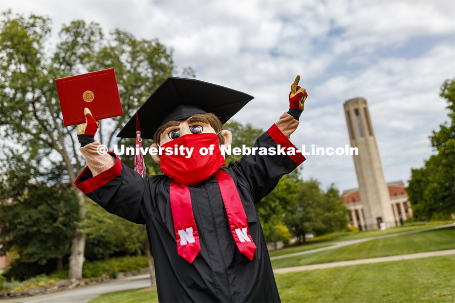 Herbie Husker has a protective mask on while he poses in front of the Mueller Bell tower while wearing a graduation cap and gown. On campus. August 5, 2020. Photo by Craig Chandler / University Communication.