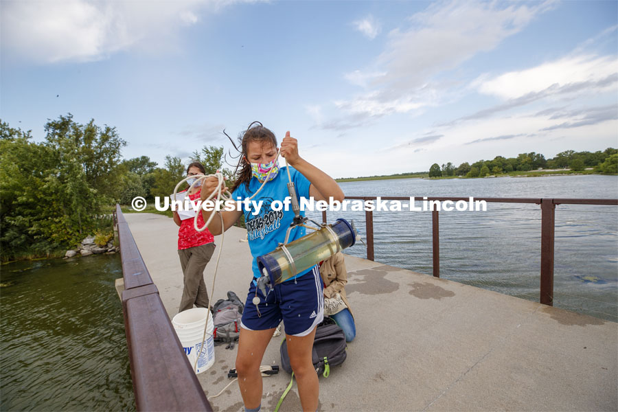 Malayna Wingert, a sophomore from Sterling, NE, lifts a water sample out of Holmes Lake as Anni Poetz and Maddie Carpenter record data. UCARE students of Professor Jessica Corman take water samples at Holmes Lake. The project is to see what makes the local lakes turn green. Is it an influx of nutrients from rain? Warm weather in the summer? They are testing what nutrients promote growth of algae and cyanobacteria in the lake, and they are testing this throughout the year. August 10, 2020. Photo by Craig Chandler / University Communication.