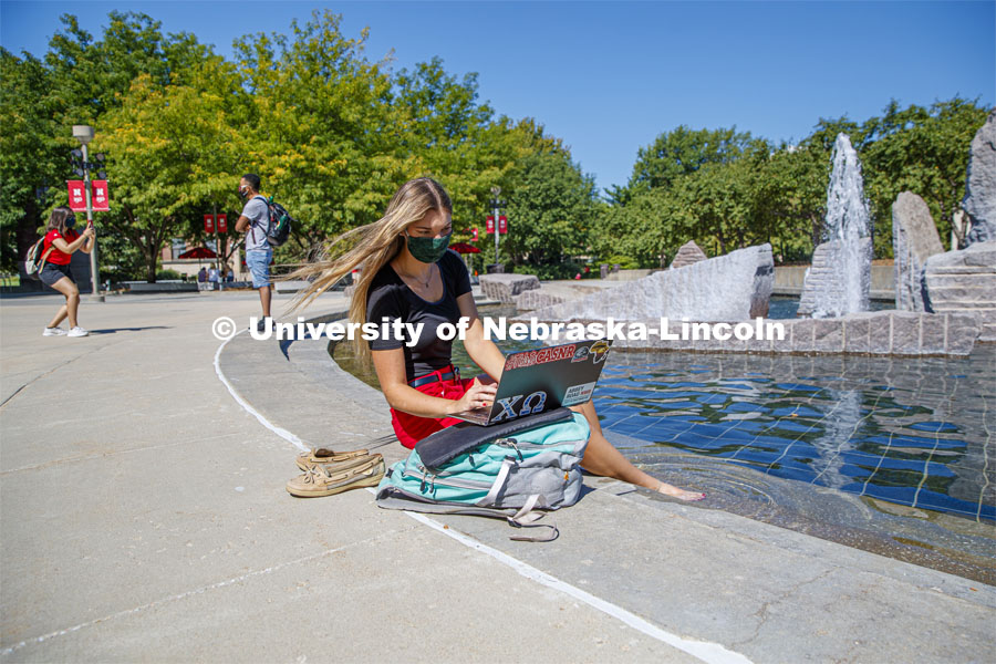 A young woman soaks her feet in the Broyhill fountain while working on her laptop computer. Photo shoot of students wearing masks and practicing social distancing. August 11, 2020 Photo by Craig Chandler / University Communication.