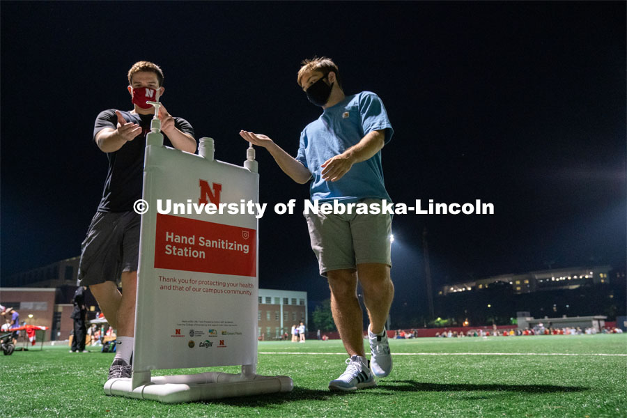 Two students make use of a hand sanitizing station while leaving Mabel Lee Fields at the conclusion of the HuskerMania Masker Singer event. August 21, 2020. Photo by Jordan Opp for University Communication.