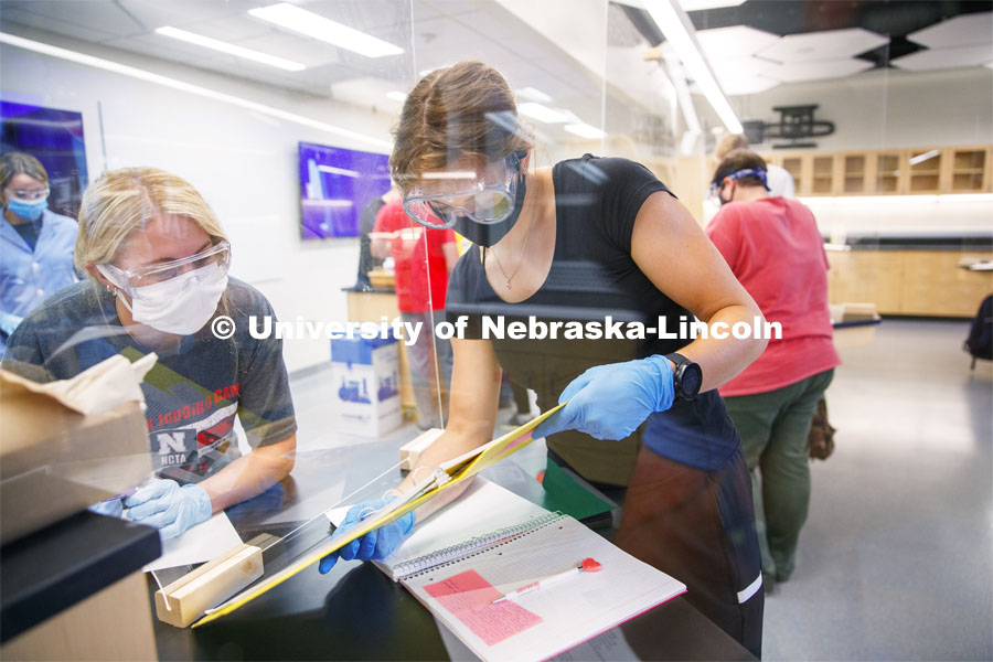 Johanna Ilves, right, and Clarissa Marron work on the report as the two lab partners are separated by an acrylic barrier in the Chemistry 105 lab. First day for in-person learning for the fall semester. August 24, 2020. Photo by Craig Chandler / University Communication.
