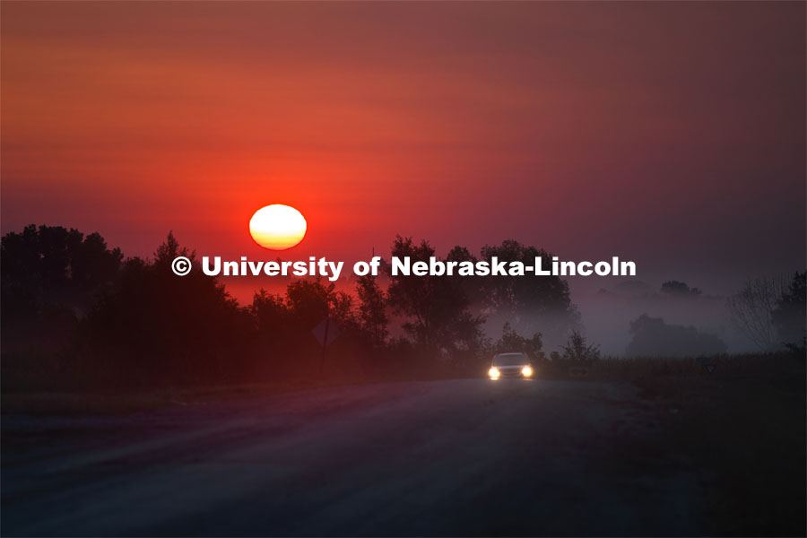 A car drives up out of the fog on a rural Nebraska road as the sun rises in the early morning sky. September 15, 2020. Photo by Craig Chandler / University Communication.