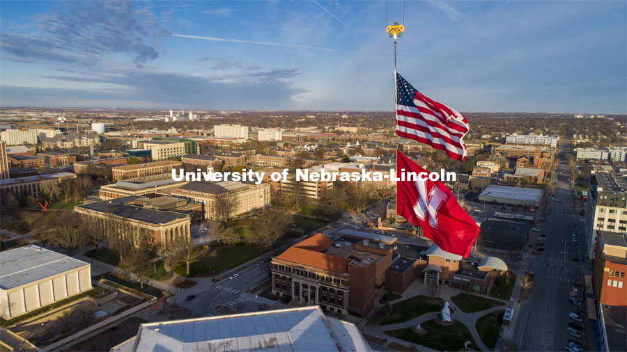 With the campus as the background, The United States and Husker flags fly on a sunny Friday afternoon from the Hausmann Construction crane being used to build the Lied Place Residences. The flags are each measure 25 x 15 feet. November 20, 2020. Photo by Craig Chandler / University Communication.