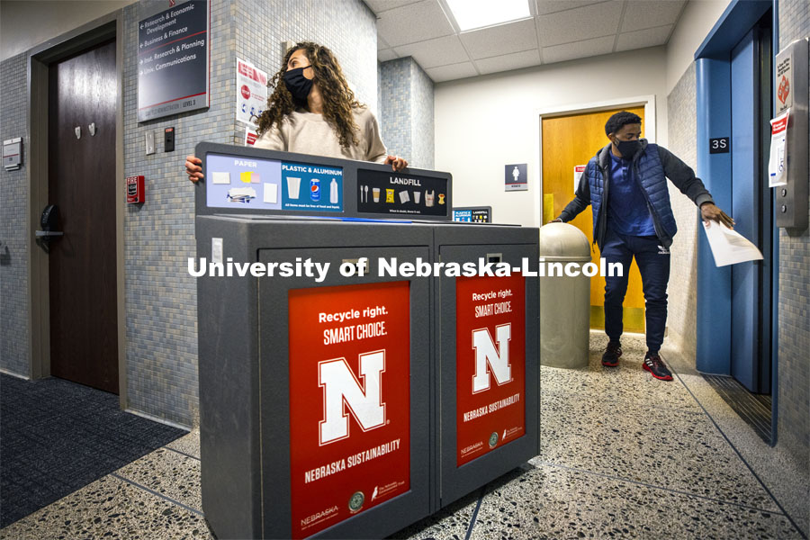 Morgan Hartman, project coordinator for recycling services, wheels a new recycling station down the hallway of Canfield Hall as student worker Damien Niyonshuti loads an old trash can onto an elevator. The Office of Sustainability is installing the new recycling stations in eight pilot buildings across City and East Campus during break. December 1, 2020. Photo by Craig Chandler / University Communication.